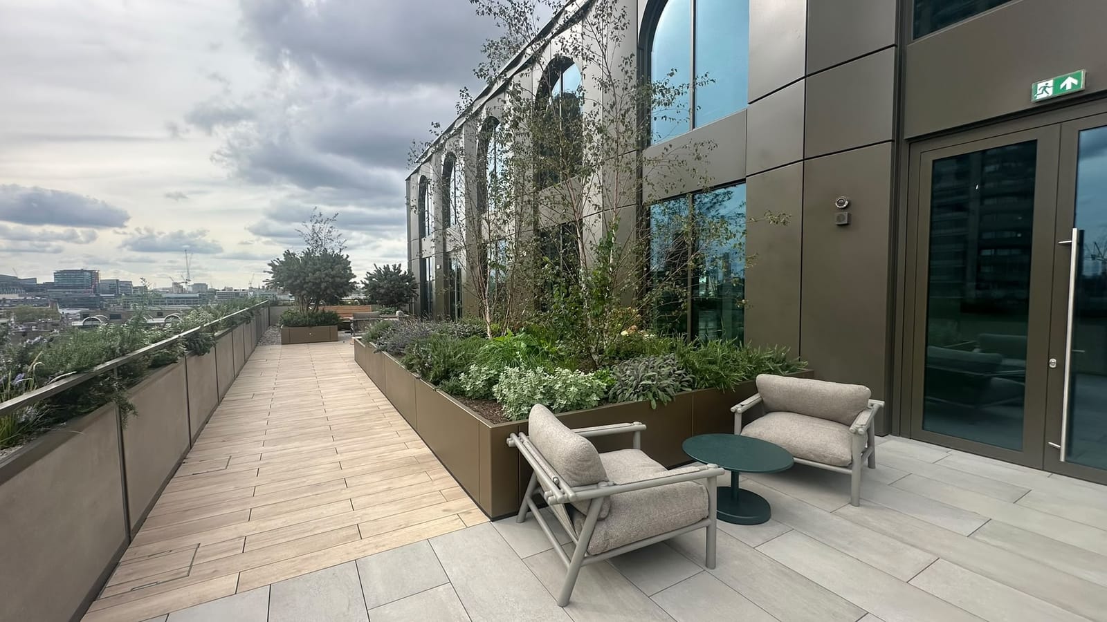 A terrace walkway with raised planters, trees and seating alongside the building at Uno Golden Lane.