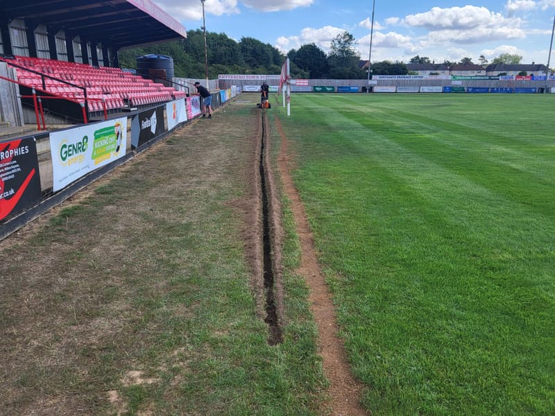 Trench cut along the edge of the pitch at Kettering Town Football Club.